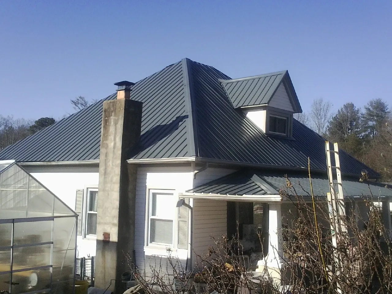 Dark blue standing seam metal roof on a white farmhouse with dormer — Slate & Tile Roof Repair by Roofing Brothers in Petal