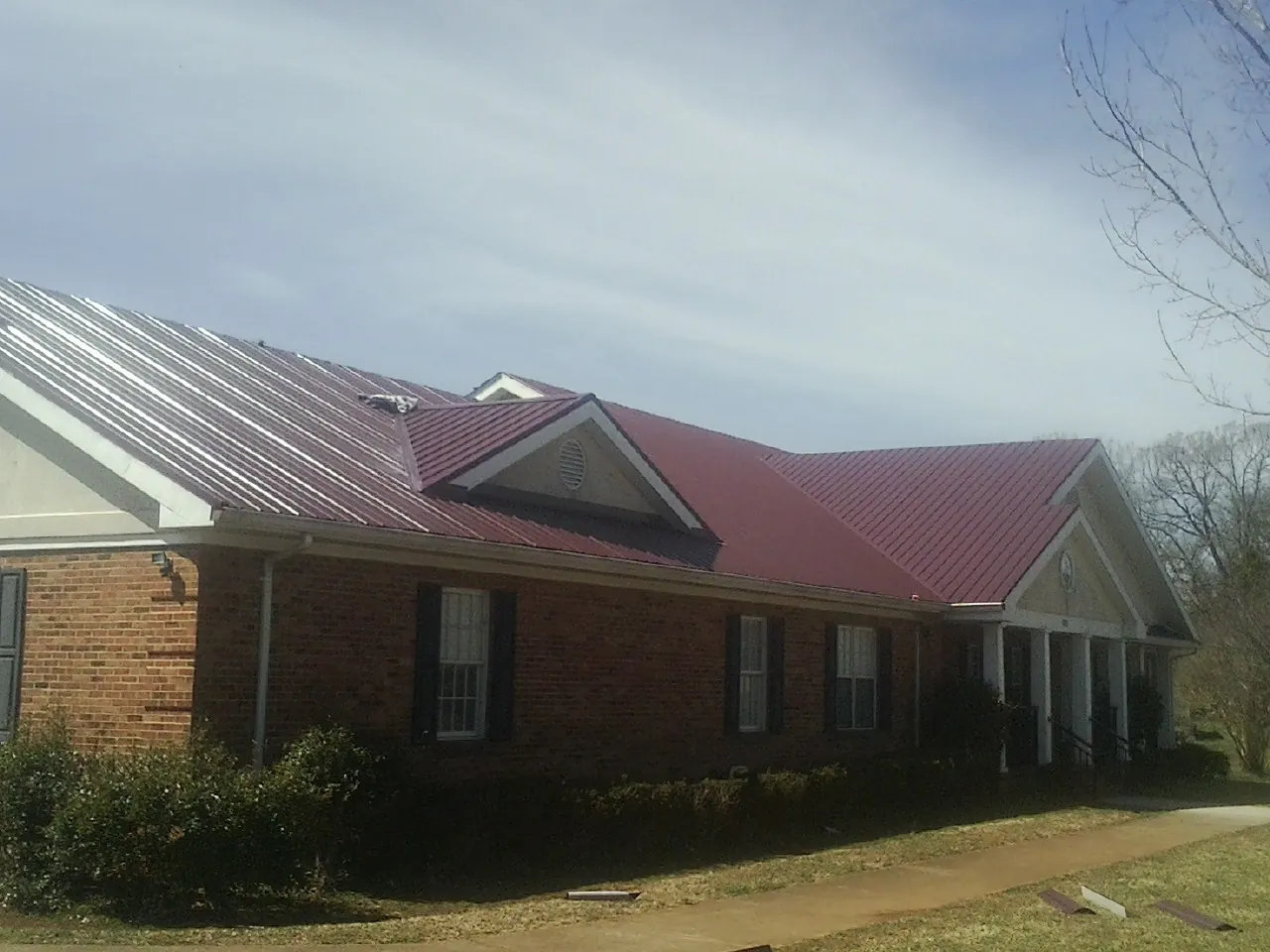 Red metal roof with gabled entries on a long brick building, from a Hail Damage Roof Repair job in Petal