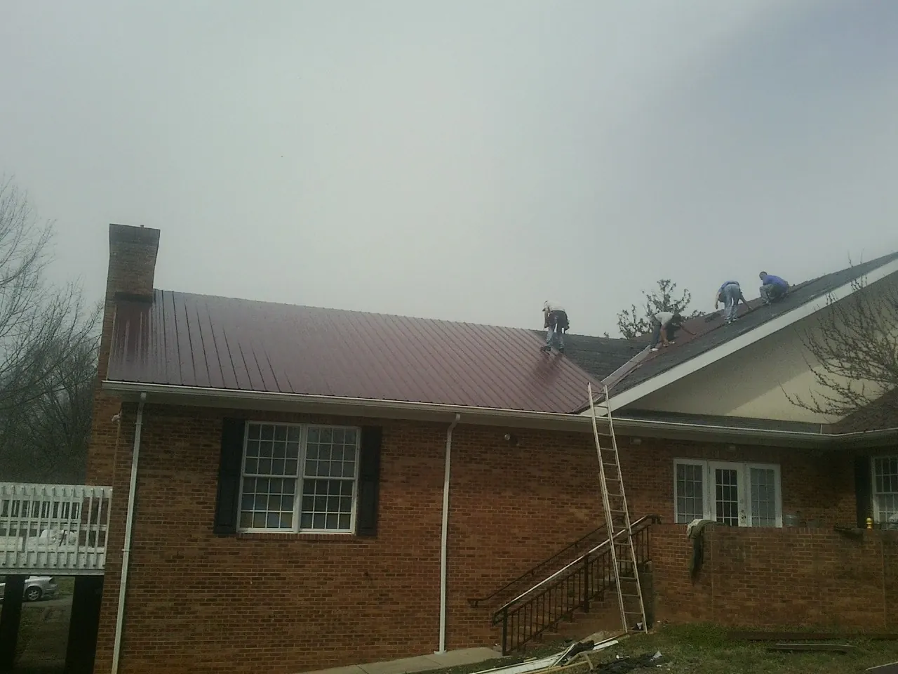 Crew setting red metal roofing panels on a brick home in Petal