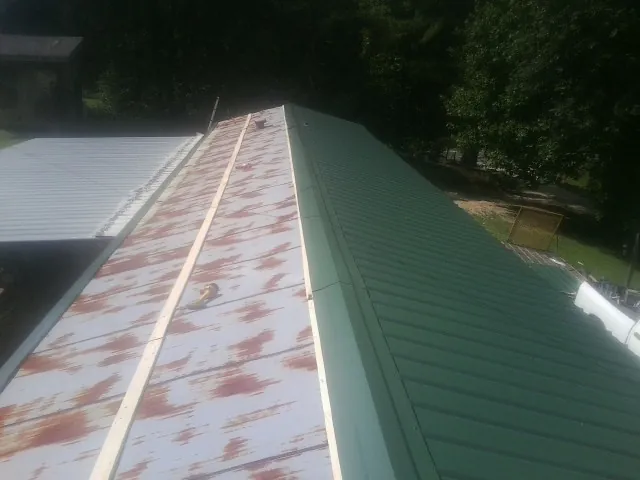 Old rusted panels beside newly installed green metal roofing — Wind Damage Roof Repair by Roofing Brothers in Petal