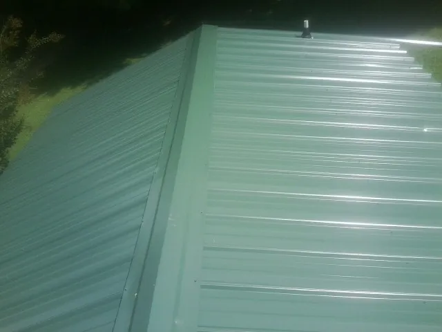 New green metal panels meeting at the ridge of a roof — Flat Roof Repair work by our crew in Petal