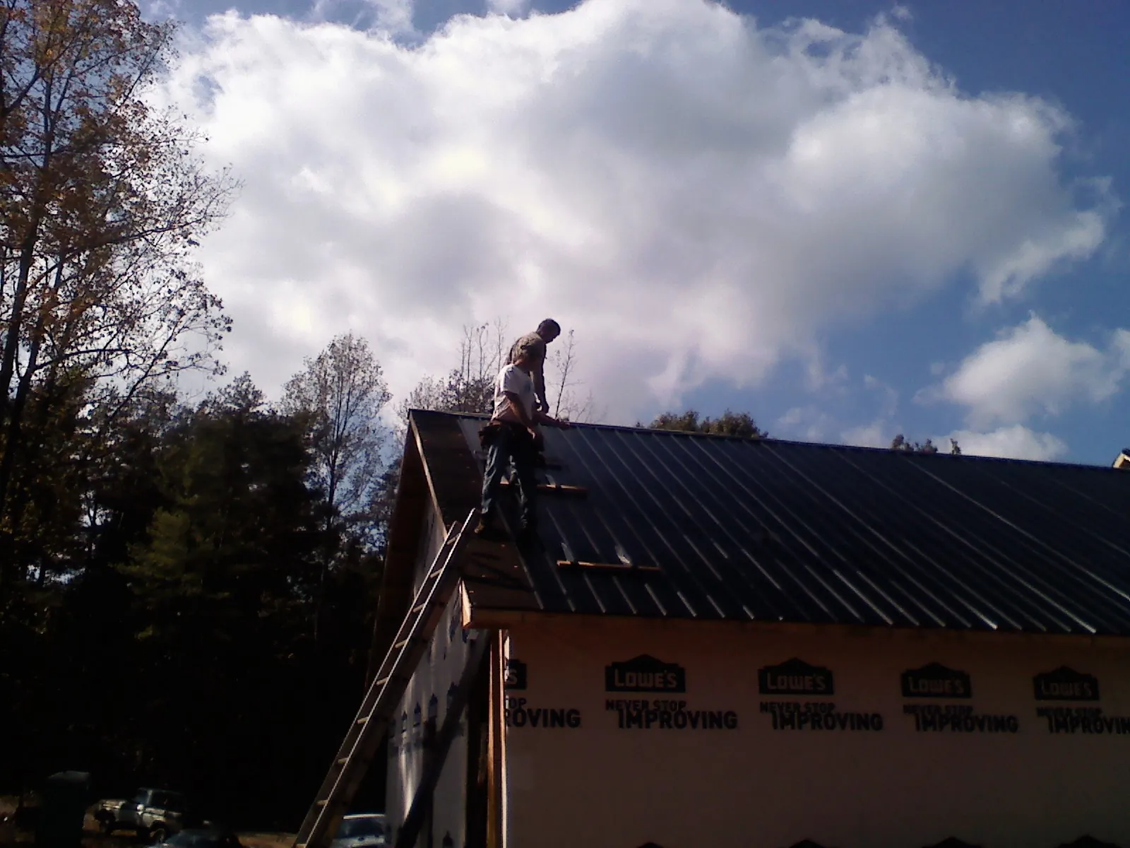 Roofer fastening dark metal panels high against a cloudy sky, from a Roof Inspection job in Petal