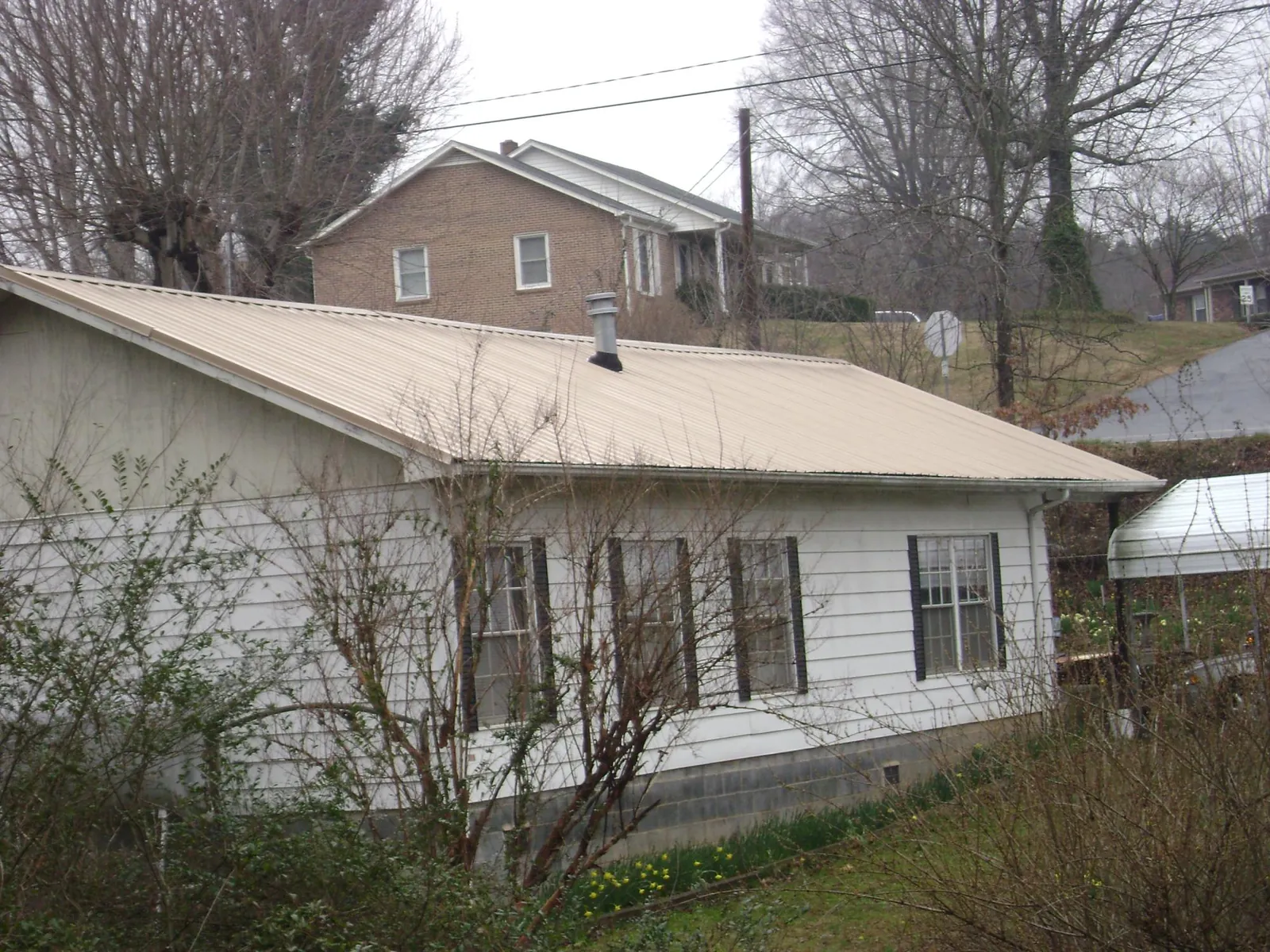 Tan metal roof on a white sided house set into a hillside — Commercial Roofing by Roofing Brothers in Petal